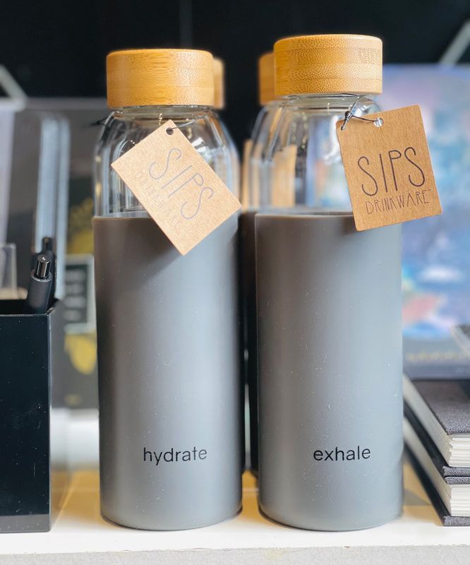 Two gray SIPS water bottles with wood caps labeled “hydrate” and “exhale” on a shelf.