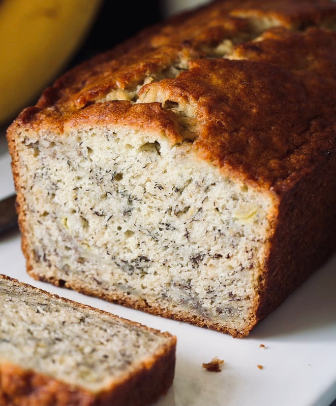 A sliced banana bread loaf with a golden brown crust and speckled white crumb on a white surface.