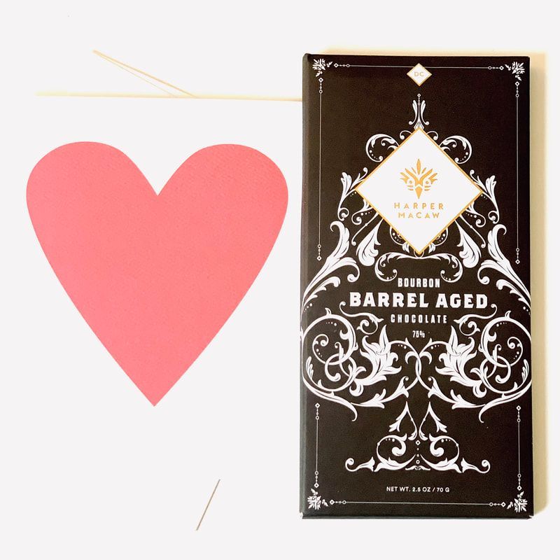 Pink heart graphic beside a dark chocolate bar package labeled “BARREL AGED CHOCOLATE.”