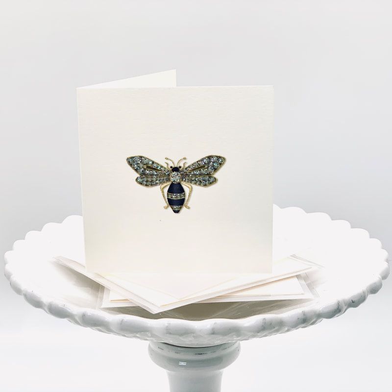 A white butterfly-winged greeting card on a scalloped pedestal dish, with a small moth illustration on the front.