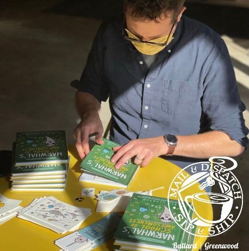 Person in a blue shirt and yellow mask sorts green booklets on a table with scattered papers.