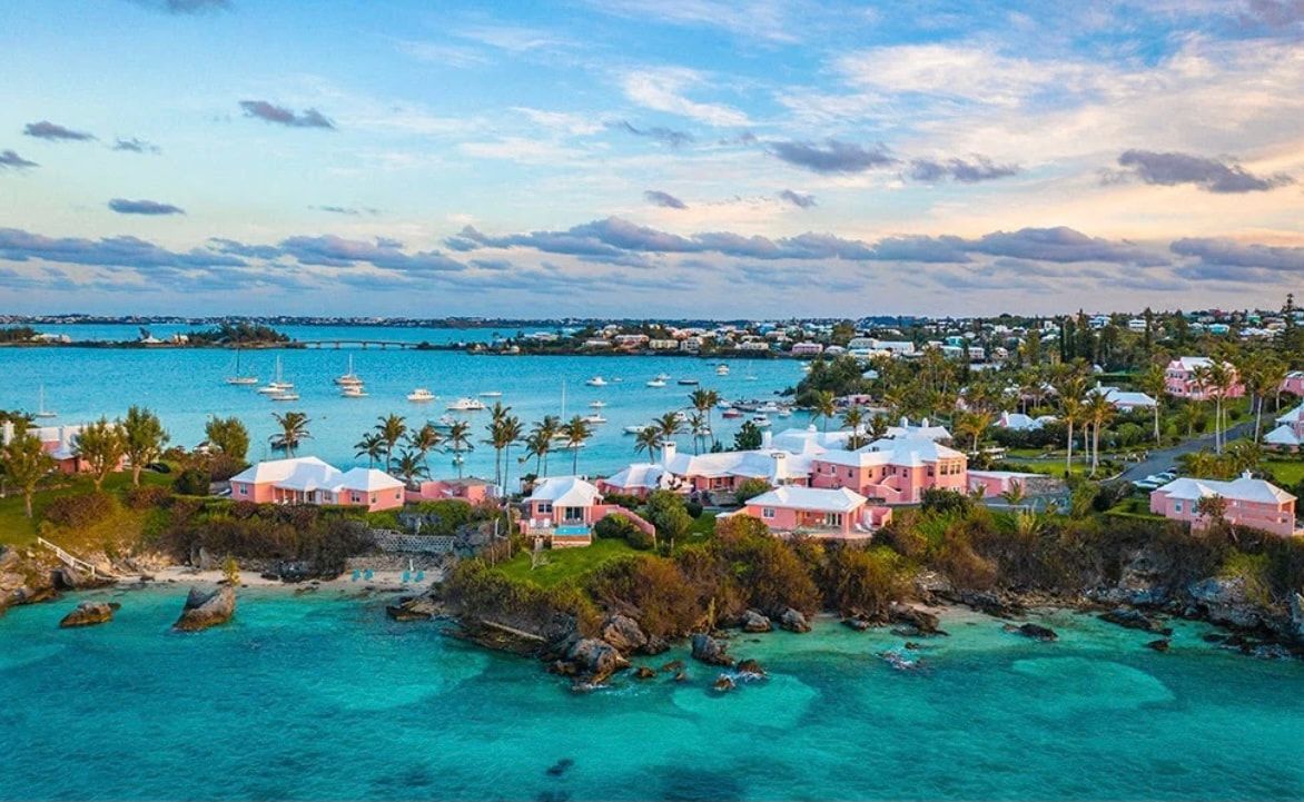 Turquoise tropical bay with white-roofed waterfront homes and boats under a cloudy pastel sky