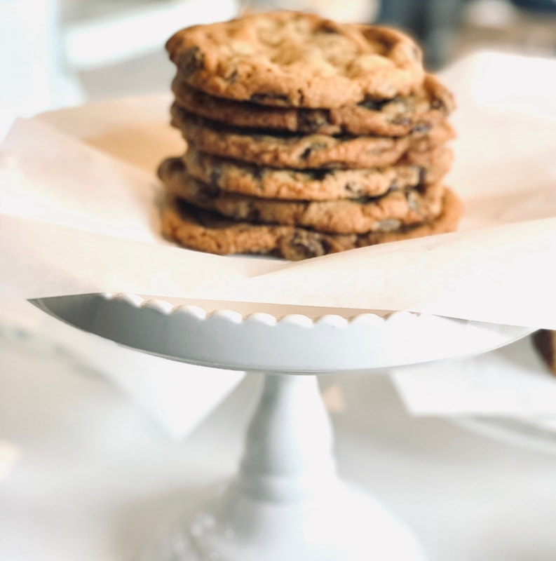 Stack of chocolate chip cookies on a white cake stand, softly lit on a white table