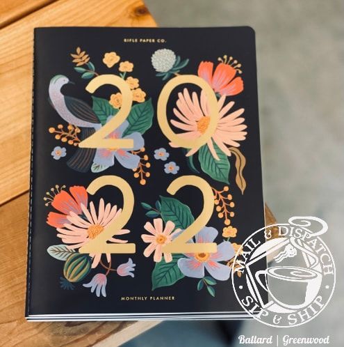 Black 2024 floral planner with large gold numbers and pastel flowers on a wooden table