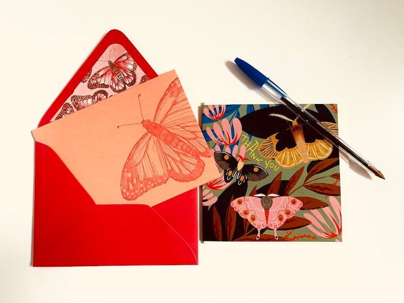 Red envelope, butterfly card, and butterfly-patterned card with blue pen on a white surface