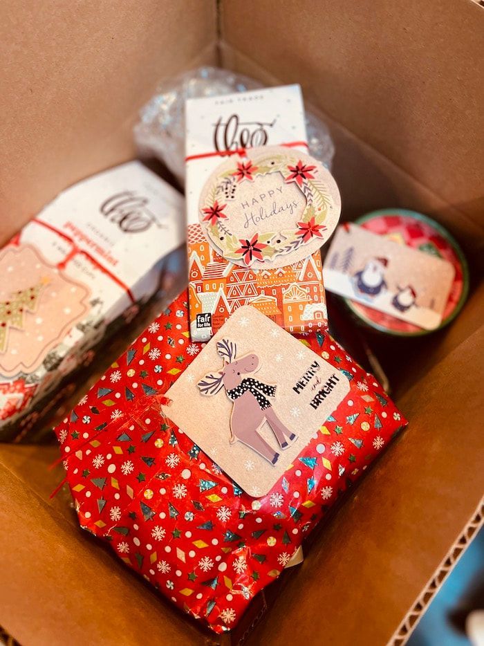 Gift-wrapped parcels in a cardboard box, including a red floral package and rolled white packages.