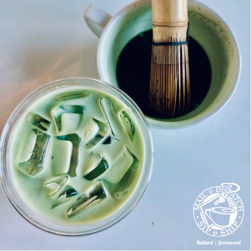Iced matcha latte in a glass beside a bamboo whisk in a green cup