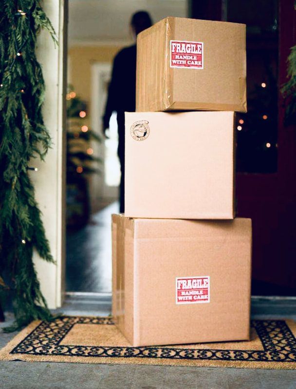 Three stacked cardboard boxes on a doorstep, with a front door and holiday wreath in the background.