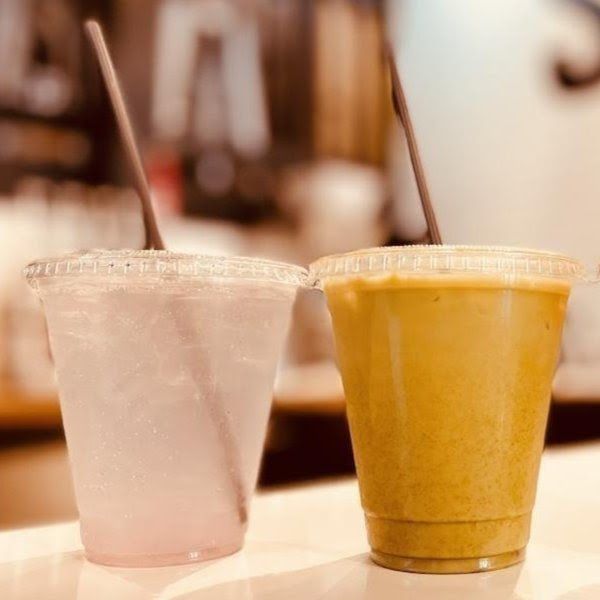 Two plastic cups of drinks on a table, one pale pink and one yellow, with straws in a café setting