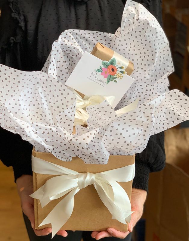 Gift box wrapped in gold ribbon and white polka-dot tissue paper with a floral card on top