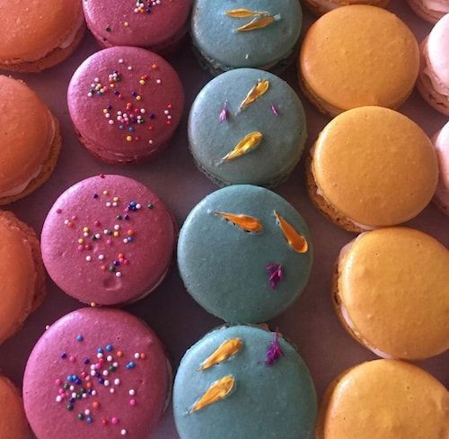 Colorful round macarons in pink, blue, and orange, some topped with sprinkles and tiny gold decorations.