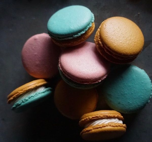 Colorful macarons in teal, pink, purple, and gold on a dark surface