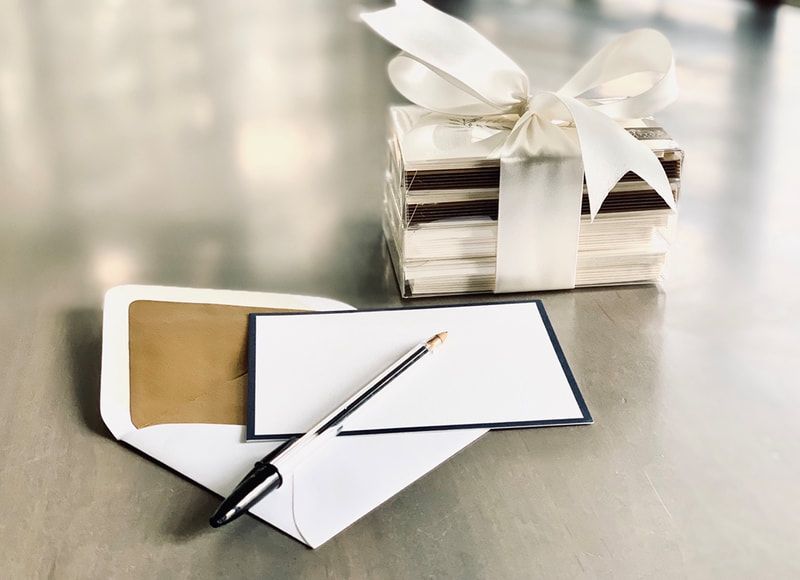 White gift box with ribbon and a pen on blank cards on a reflective surface