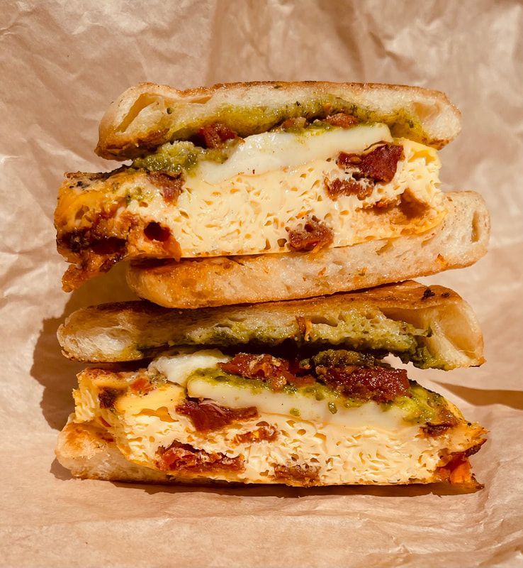 Stacked toasted sandwich halves with melted cheese, green pesto, and sun-dried tomatoes on brown paper