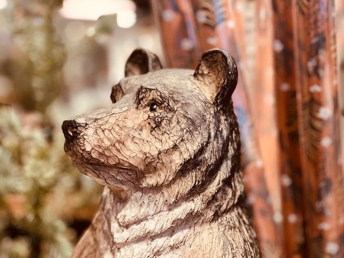 Small carved bear figurine with a textured brown finish, shown in close-up against a blurred background