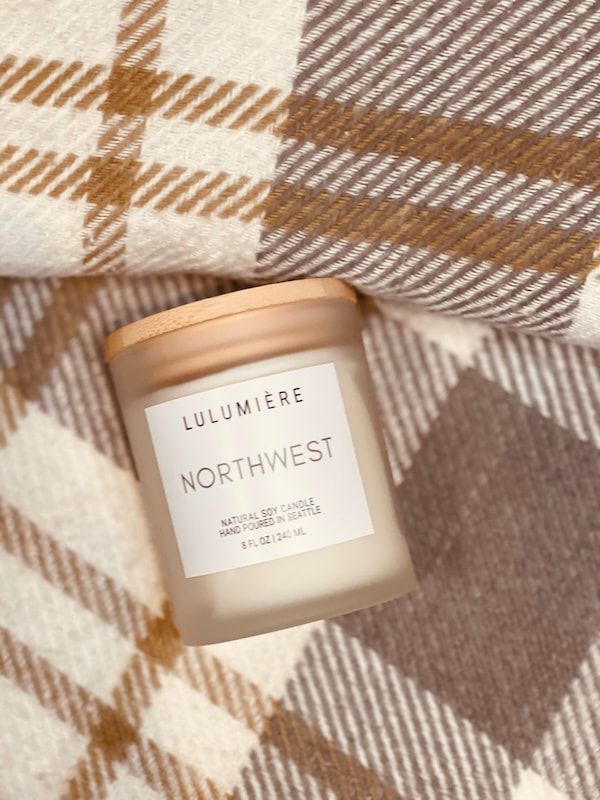 Lit candle jar labeled “Illuminet Northwest” on a beige and brown plaid blanket