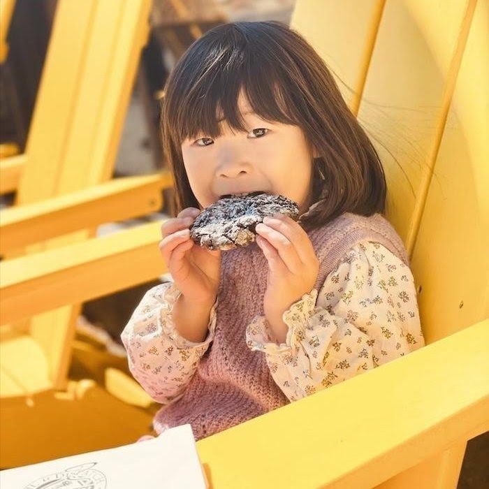 Child holding a powdered donut on a bright yellow bench, with a playful expression