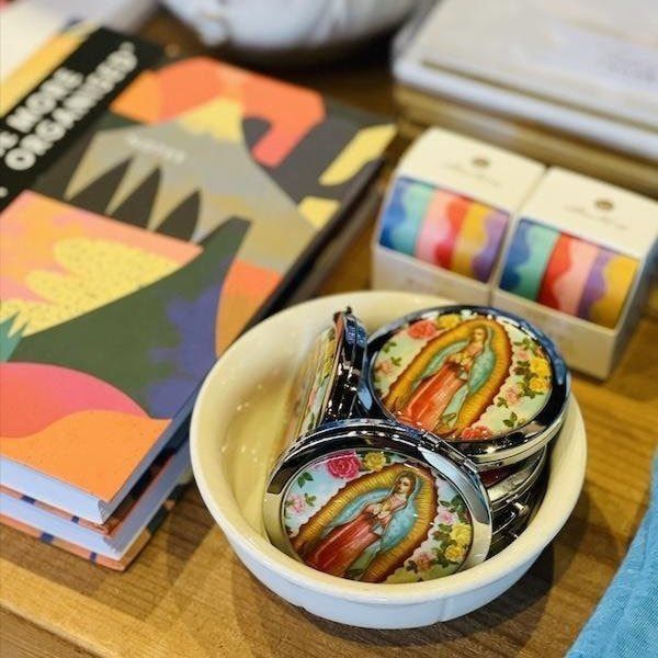 Colorful notebooks and enamel pins displayed on a wooden table in a shop.