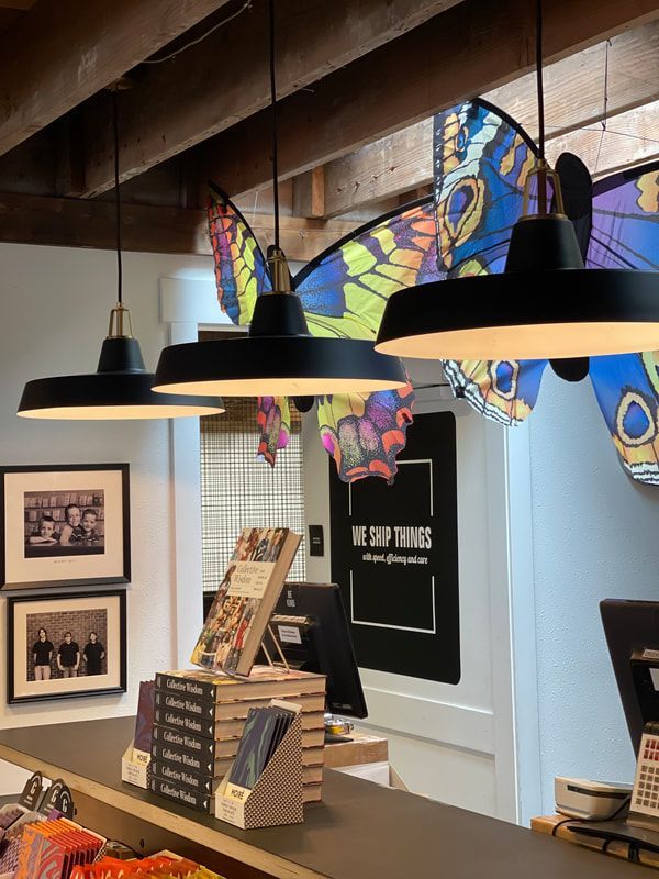 Interior of a shop with butterfly wall art, hanging black lamps, and a display of books and framed prints.