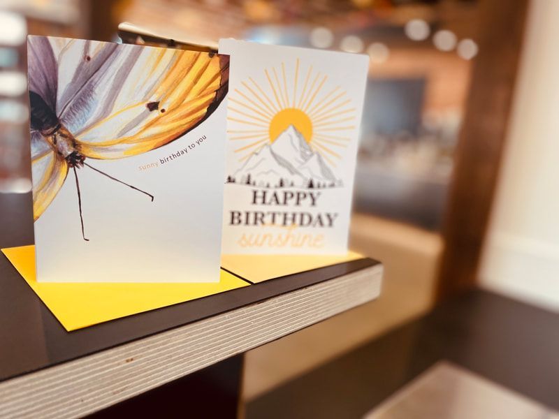 Birthday greeting card with butterfly and sunburst designs, reading “Happy Birthday,” on a wooden table