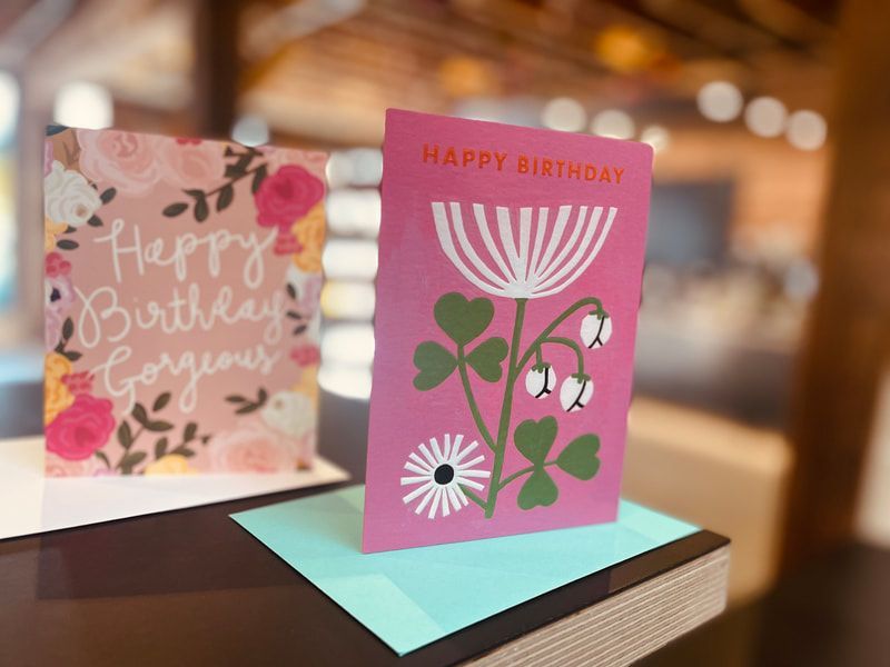 Two birthday cards on a table, one pink floral card in front and one pastel card behind.