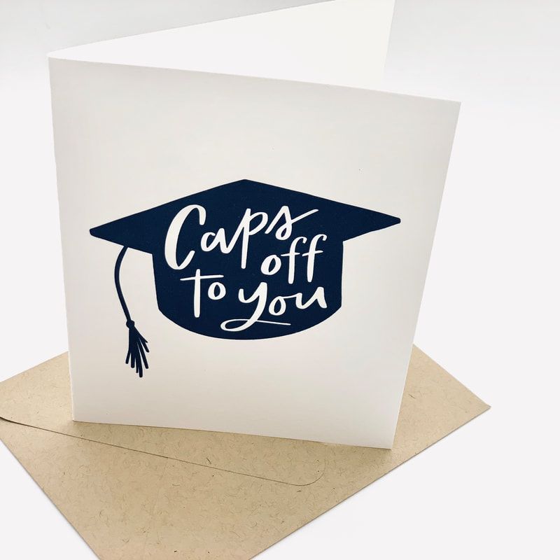 White graduation card with navy cap graphic and the words “Caps off to you” on a kraft envelope