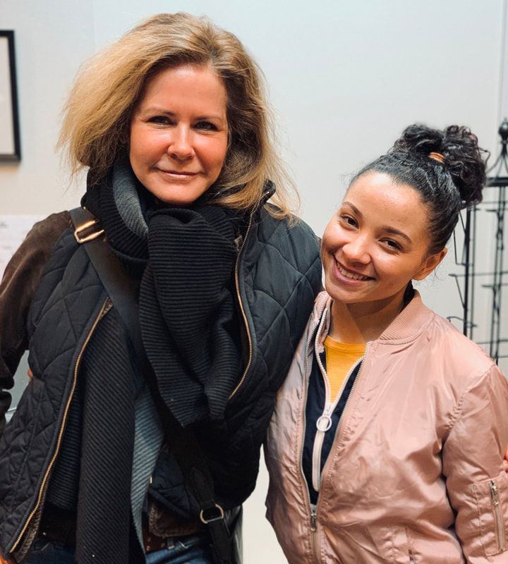 Two smiling women standing together indoors, wearing black and pink jackets.