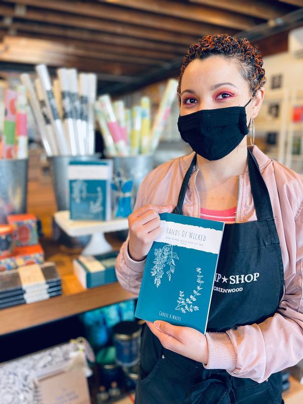 Woman in a mask holding a blue notebook inside a shop with bookshelves and plants