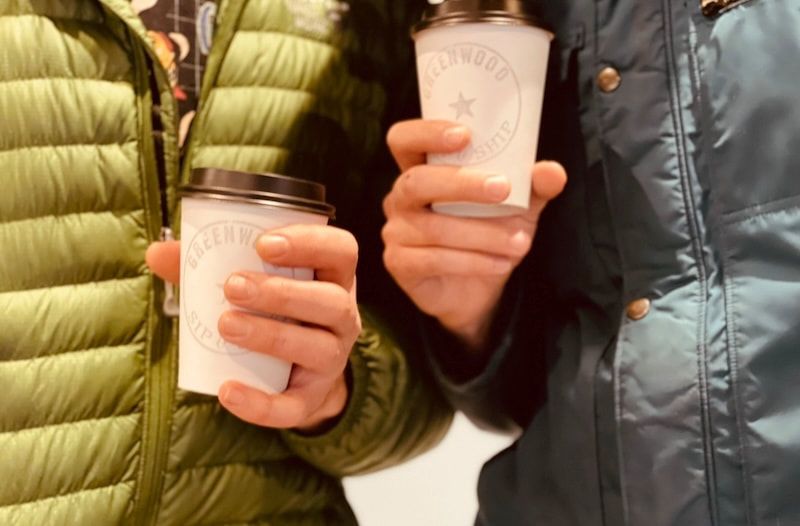 Two people in puffer jackets holding lidded takeaway coffee cups close together