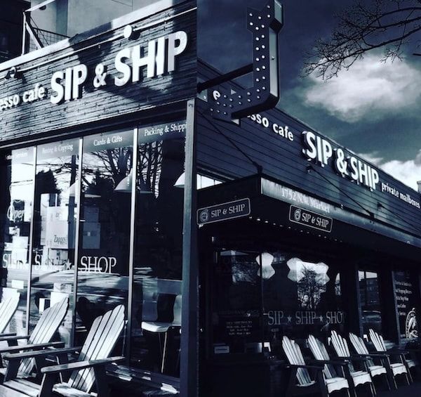 Black-and-white storefront of a cafe named “SIP & SHIP” with outdoor chairs and cloudy sky