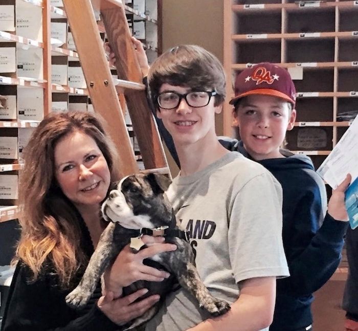 Woman and two youths smiling with a small dog in a store or warehouse setting