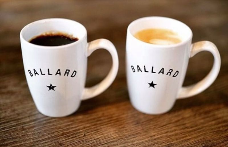 Two white BALLARD mugs on a wooden table, one filled with coffee and one with a latte.