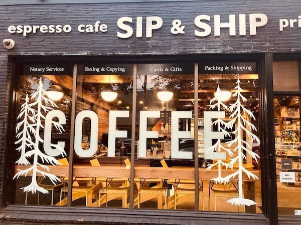 Coffee shop storefront with large “COFFEE” sign, white tree graphics, and “SIP & SHIP” above the windows