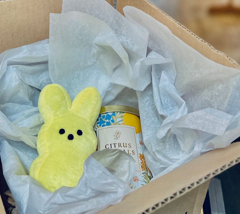 Yellow plush bunny and a citrus can nestled in tissue paper inside a cardboard gift box