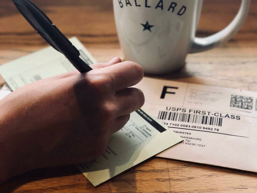Hand writing on a form beside a coffee mug on a wooden desk