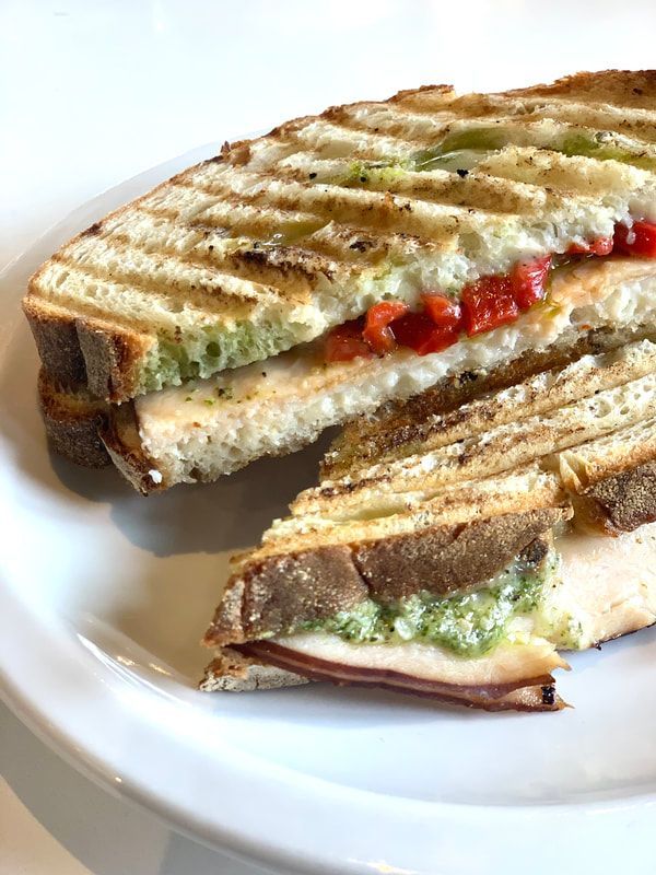 Grilled sandwich on a white plate, cut in half, with melted cheese and tomato filling.