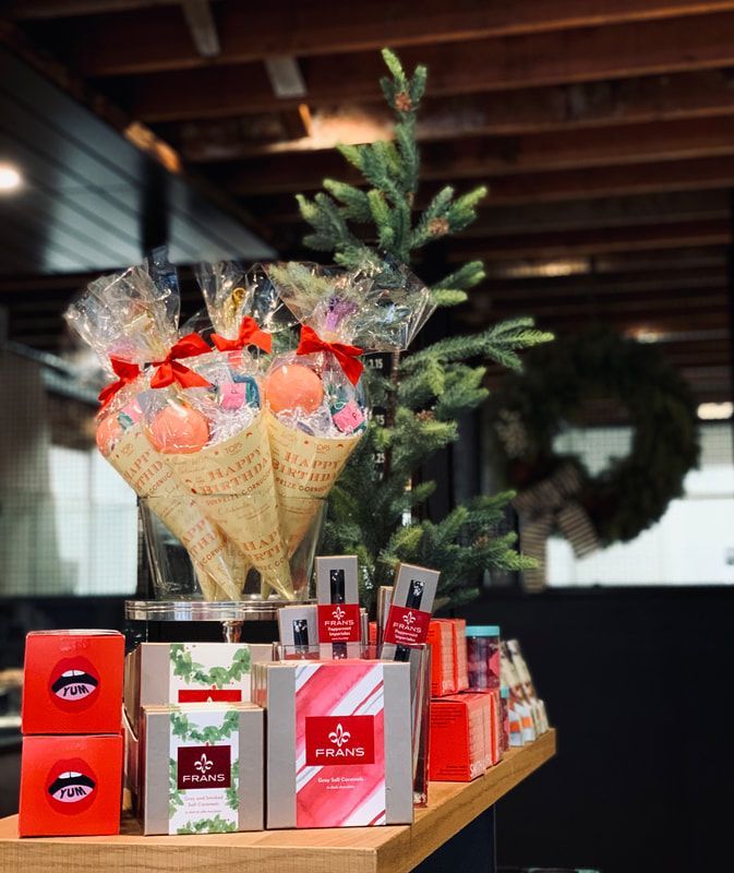 Gift baskets and boxes arranged on a table with a decorated Christmas tree in a festive indoor setting