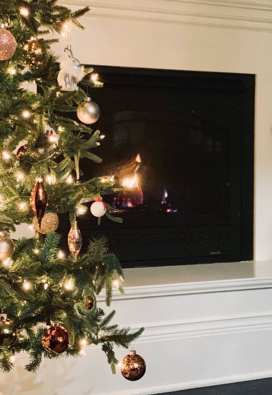 Decorated Christmas tree beside a glowing fireplace in a cozy living room