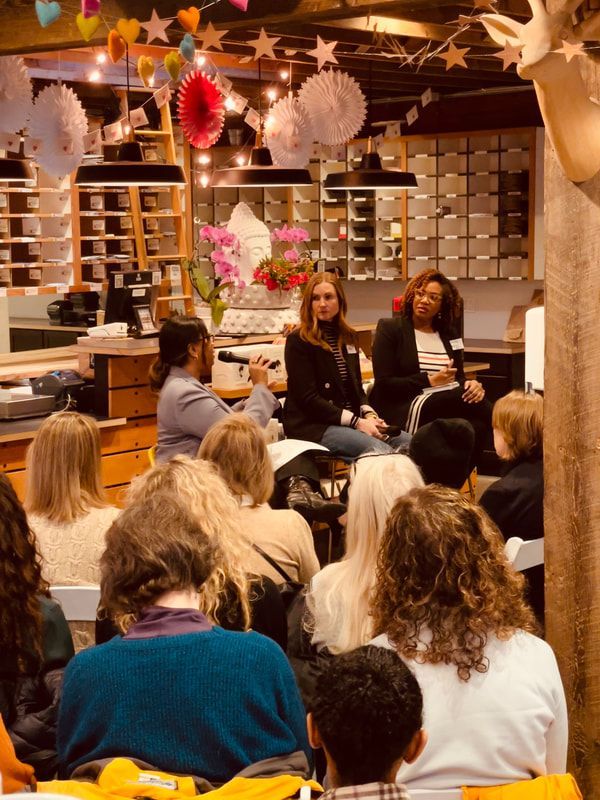 Panel discussion in a cozy café, with seated audience and three speakers at the front under hanging decorations