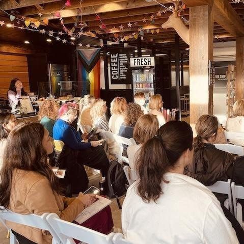 Audience seated in a rustic café listening to a speaker near a “COFFEE” sign