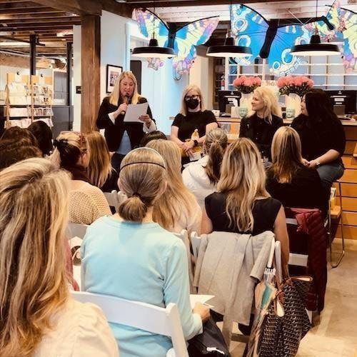 Panel discussion in a bookstore, with four speakers addressing a seated audience under butterfly decorations