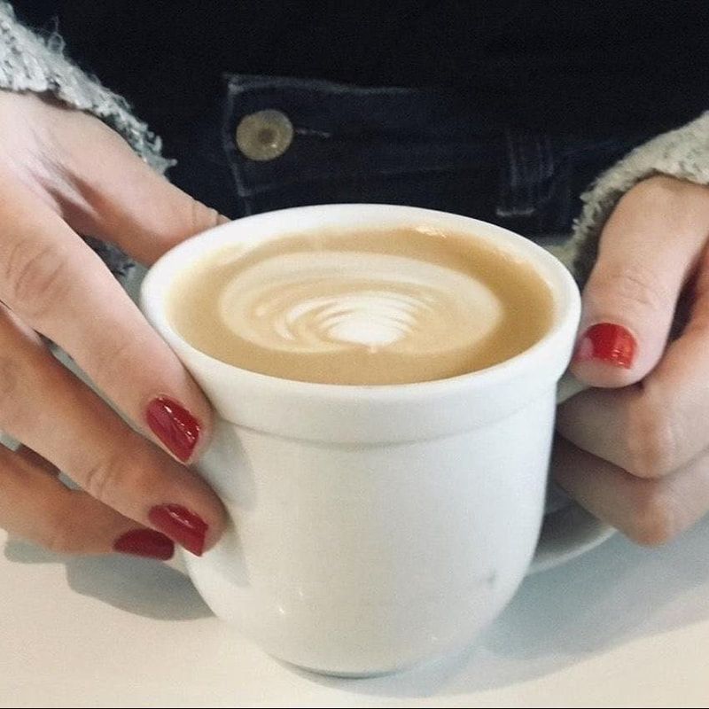 Hands holding a white cup of latte with heart latte art on a table