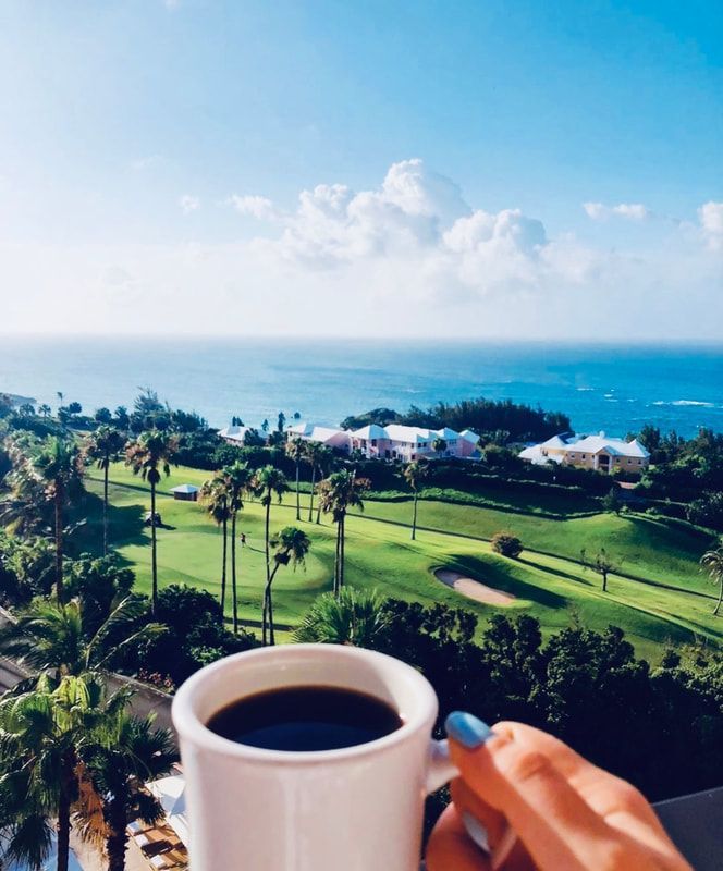Hand holding a coffee mug overlooking a sunny golf course and ocean view