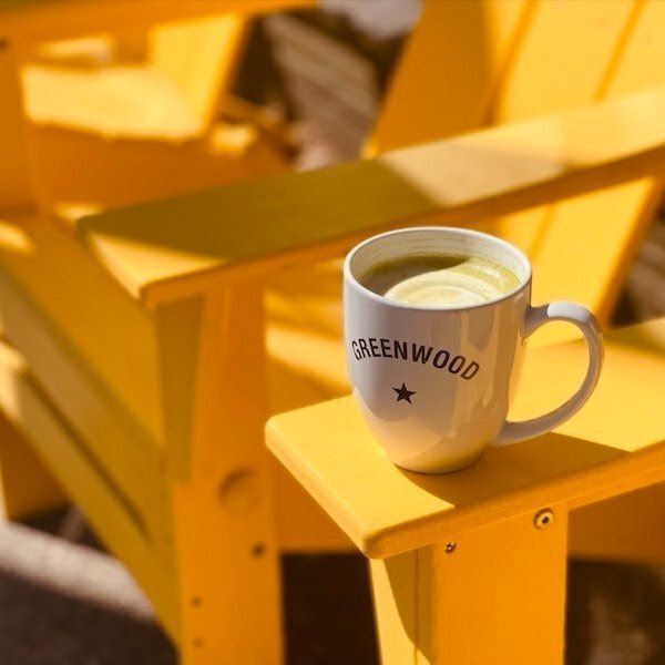 White coffee mug on a yellow bench outdoors, with blurred yellow chairs in the background