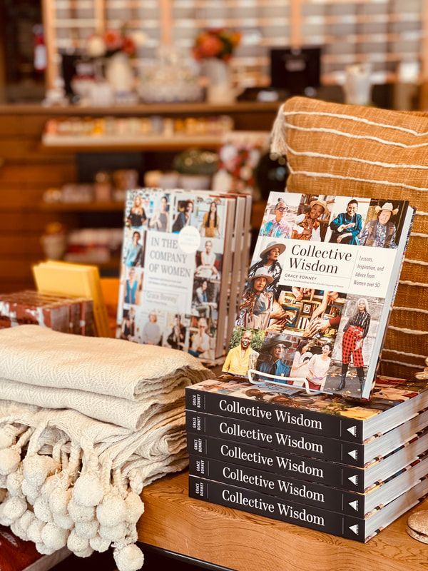 Stacked “Collective Wisdom” books on a wooden table with folded blankets in a cozy shop display