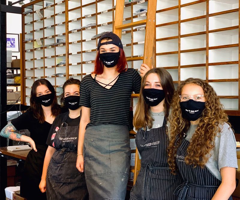 Five masked people standing together indoors in front of a wall of shelves