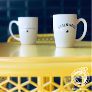Two white mugs on a yellow table, one labeled Greenwoods.