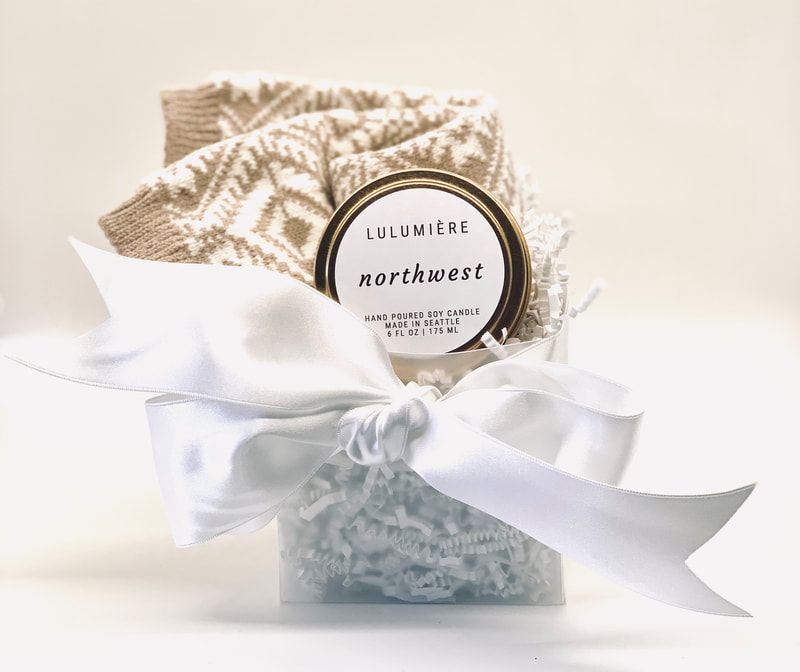 Gift box with folded beige blanket, white ribbon, and round “Lumière Northwest” label on a light background