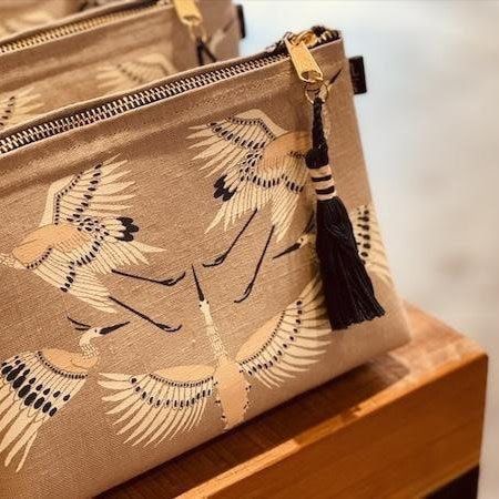Beige floral clutch bag with a black tassel, resting on a wooden surface.