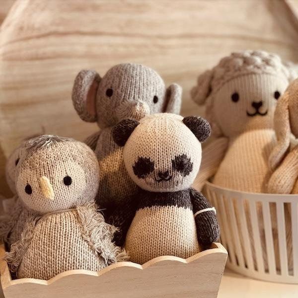 Four knitted stuffed animals on a wooden shelf, including a panda, owl, elephant, and teddy bear.